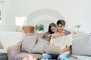 Happy young couple looking laptop relax on sofa in living room watch video on laptop together