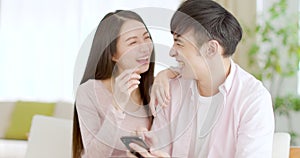 Happy young couple  looking at mobile phone in living room at home