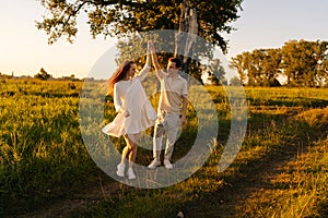 Happy young couple in love dancing together on green meadow in summer evening during sunset with soft sunlight