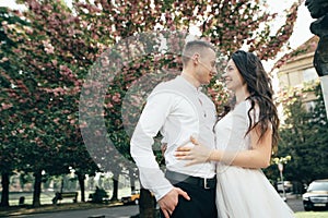 Happy young couple in love enjoys spring day, loving man holding on hands his woman carefree walking at park