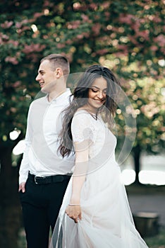 Happy young couple in love enjoys spring day, loving man holding on hands his woman carefree walking at park