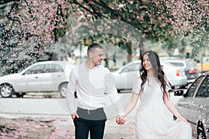 Happy young couple in love enjoys spring day, loving man holding on hands his woman carefree walking at park