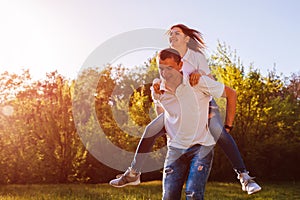 Young couple in love having fun in spring forest. Man rides his girlfriend on back at sunset.