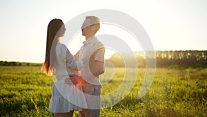 Happy young couple in love hugging, kissing and holding hands on background of sunset in summer field. Romantic date