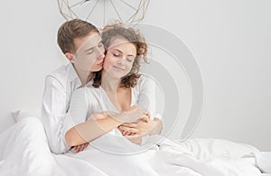 Happy young couple in love sitting hugging on the bed at home