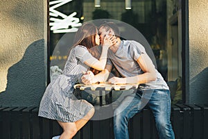 Happy young couple in love teenagers friends dressed in casual style kissing in street cafe