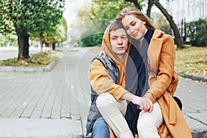 Happy young couple in love teenagers friends dressed in casual style sitting together on the autumn city street