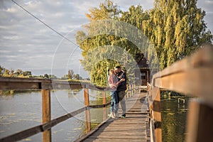 Happy young couple in love walking in bridge at sunset. Man embracing and going to kiss sensual woman