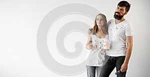 Happy young couple in love in white t-shirts makes renovations, updating the painting of the walls, getting ready to