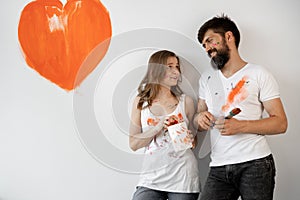 Happy young couple in love in white t-shirts making renovations, updating the painting of the walls, getting ready to