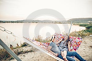 Happy young couple lying on a hammock near the beach at sunset, handsome man and beautiful woman spending summer vacation outdoors