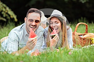 Happy young couple lying next to each other on a picnic blanket and eating watermelons