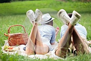 Happy young couple lying next to each other and eating watermelons, picnic in a park. View from behind