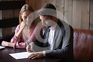 Happy young couple making deal, husband signing contract at meeting