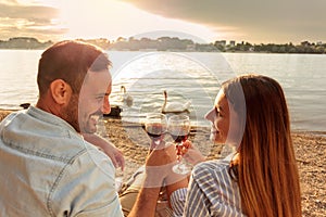 Happy young couple making a toast with red wine. Enjoying picnic at the beach