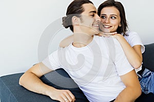 Happy young couple of man and woman embracing look at each other sitting on couch in living room