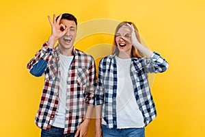 Happy young couple, man and woman, make a good gesture, show a symbol of approval, on a yellow background