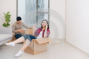 Happy young couple moving in their new apartment, having fun and riding in cardboard boxes at new home