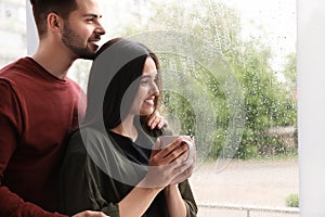 Happy young couple near window on rainy day