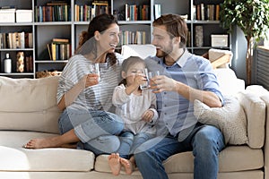 Happy young couple parents teaching little daughter drinking clear water.