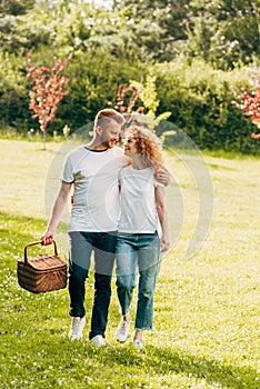 happy young couple with picnic basket walking on lawn