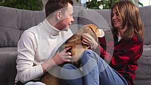Happy young couple playing and relaxing with pet dog beagle at home. Portrait of caucasian man and woman in love feeding
