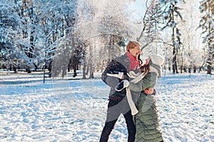 Happy young couple playing with snow in winter park. Man and woman having fun outdoors.