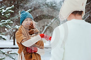 Happy young couple playing on winter walk, throwing snowballs and having fun outdoor