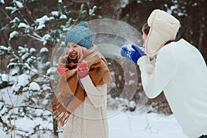 Happy young couple playing on winter walk, throwing snowballs and having fun outdoor