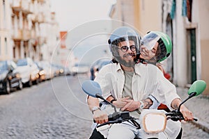 Happy young couple in protective hats are riding on vintage scooter in the Lisbon street