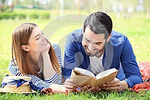 Happy young couple reading book in park on spring day