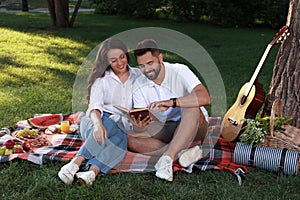 Happy young couple reading book on plaid in park. Summer picnic