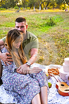 Happy young couple relaxing and having picnic in park. Peaceful sweet couple enjoying dinner in park. Man and woman sitting on