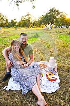 Happy young couple relaxing and having picnic in park. Peaceful sweet couple enjoying dinner in park. Man and woman sitting on