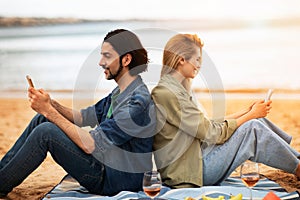 Happy Young Couple Relaxing With Smartphones On The Beach Outdoors