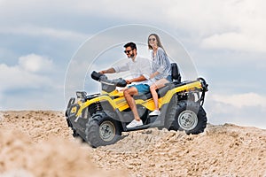 happy young couple riding all-terrain vehicle in desert