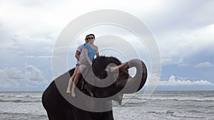 Happy young couple is riding on an elephant with trunk up on the background of a tropical ocean