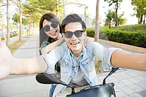 Happy young couple riding scooter and making selfie photo