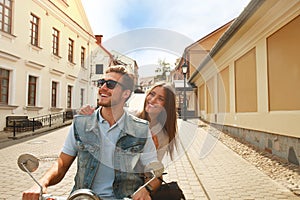 Happy young couple riding scooter in town. Handsome guy and young woman travel. Adventure and vacations concept.