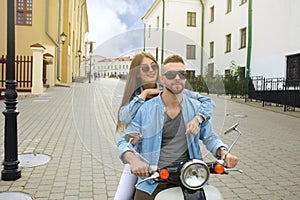 Happy young couple riding scooter in town. Handsome guy and young woman travel. Adventure and vacations concept.