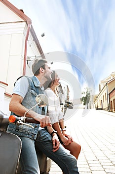 Happy young couple riding scooter in town. Handsome guy and young woman travel. Adventure and vacations concept.