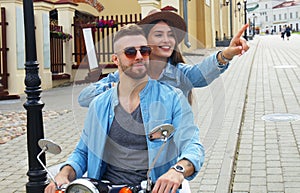 Happy young couple riding scooter in town. Handsome guy and young woman travel. Adventure and vacations concept.