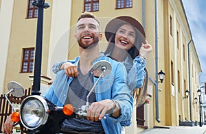 Happy young couple riding scooter in town. Handsome guy and young woman travel. Adventure and vacations concept.