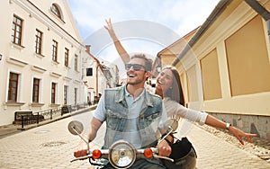 Happy young couple riding scooter in town. Handsome guy and young woman travel. Adventure and vacations concept.