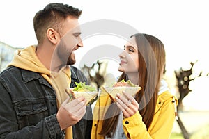 Happy young couple with sandwiches on city street