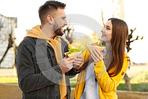 Happy young couple with sandwiches on city street