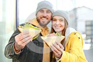 Happy young couple with sandwiches on city street