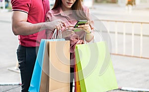 Happy young couple of shoppers walking in the shopping street towards and holding colorful shopping bags in hand and use a