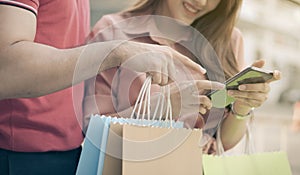 Happy young couple of shoppers walking in the shopping street towards and holding colorful shopping bags in hand and use a