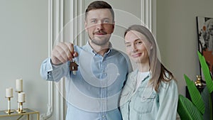 Happy young couple show new own house keys. Young smiling couple showing keys to new home hugging looking at camera.